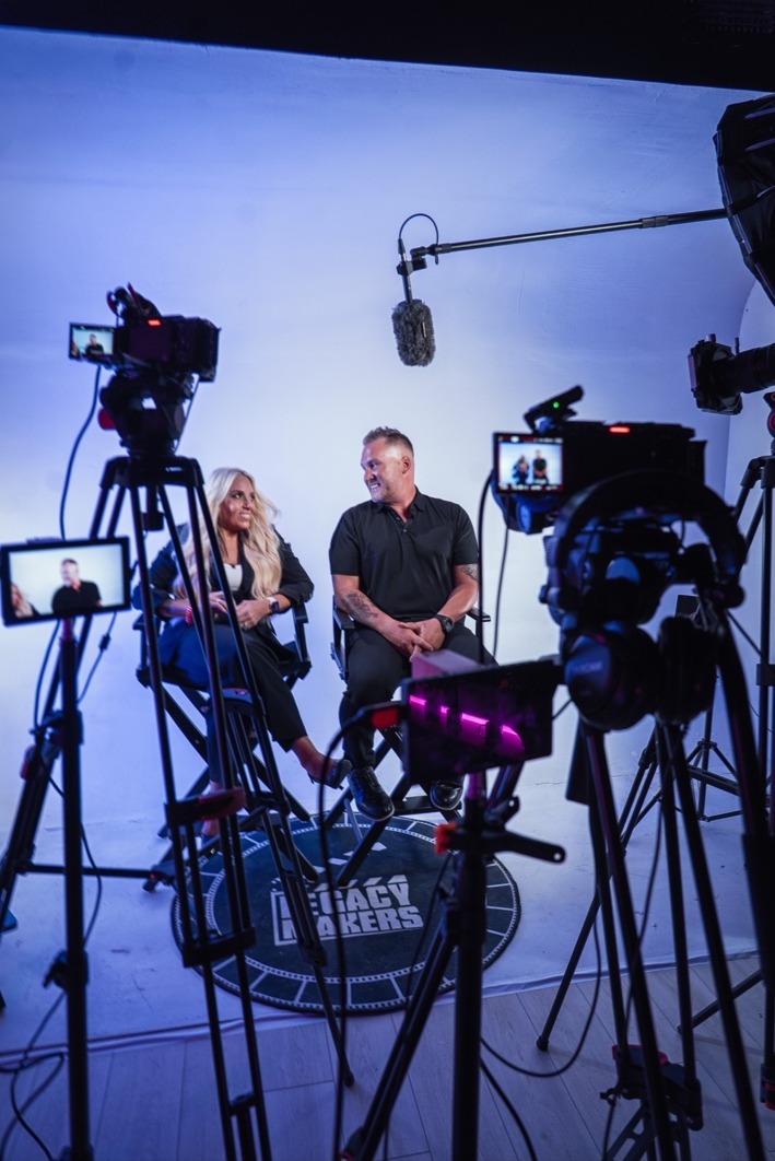 Laura Roark and Jamie Hale being interviewed on set with production cameras in the foreground