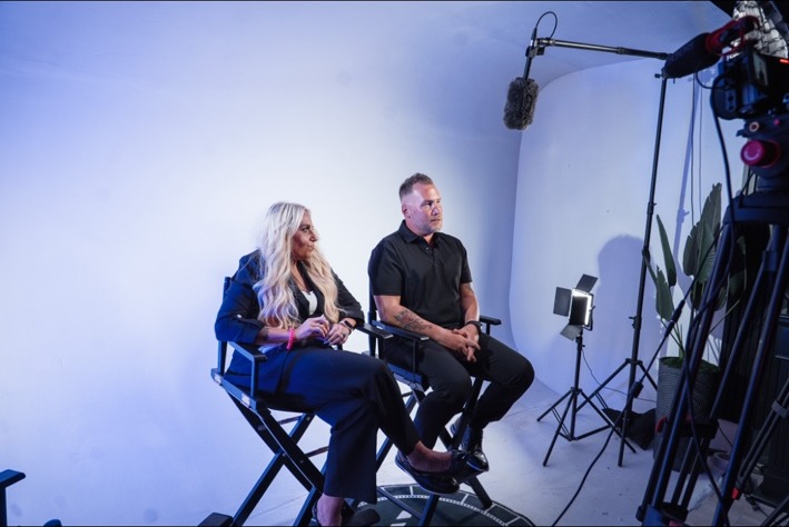 Laura Roark and Jamie Hale seated on set during filming, surrounded by professional cameras and studio lighting