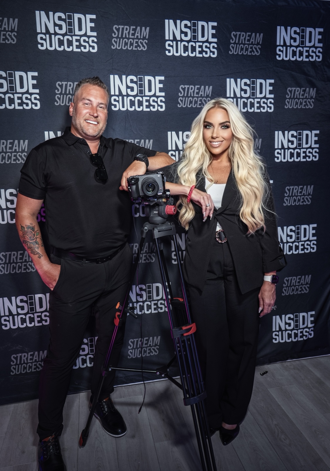 Laura Roark and Jamie Hale standing beside a professional video camera in front of the Inside Success step-and-repeat